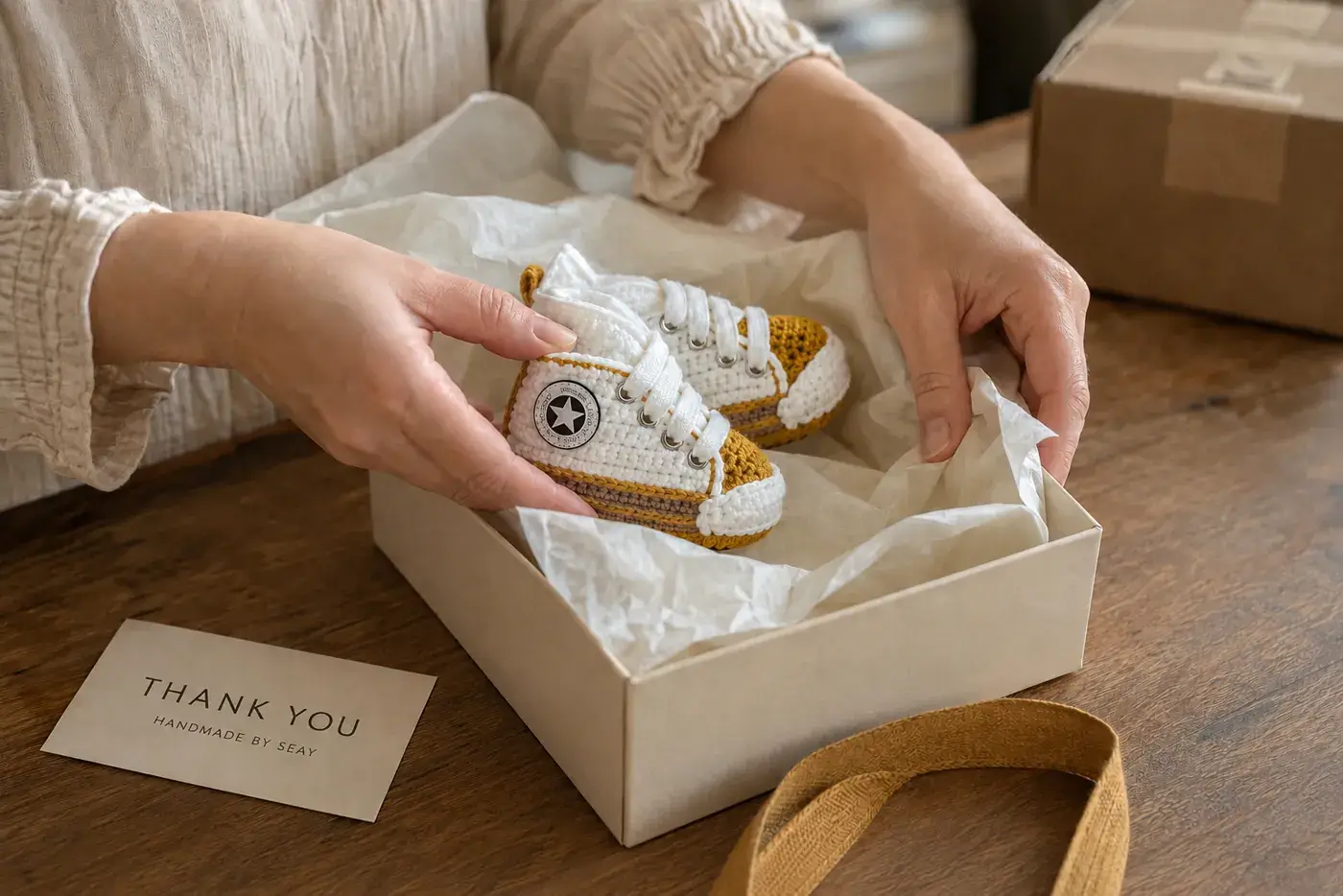 Handmade crochet baby booties being placed in a By Seay gift box